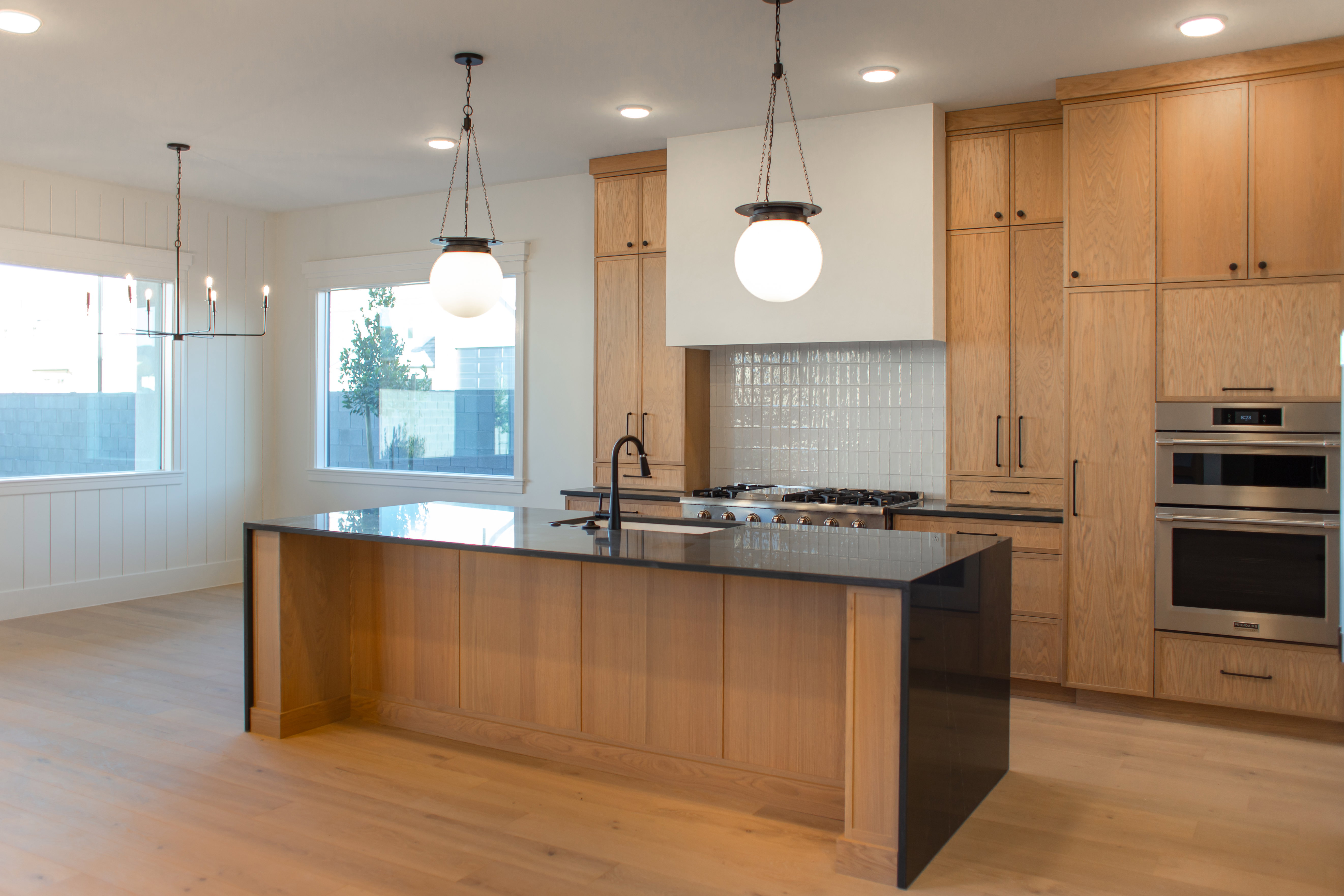 Kitchen featuring dark stone counters, light wood finished floors, a kitchen island with sink, stainless steel double oven, and wood walls
