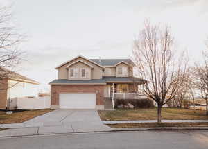 Traditional-style house with covered porch, driveway, a garage, brick siding, and a gate