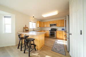 Kitchen featuring a breakfast bar, stainless steel appliances, light countertops, a peninsula, and light wood-style flooring