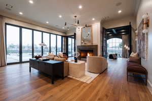 Living area with hardwood / wood-style flooring, a warm lit fireplace, crown molding, and hanging lights
