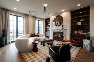 Living room with built in shelves, hardwood / wood-style floors, a high end fireplace, and recessed lighting