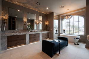 Full bath with double vanity, a chandelier, a freestanding bath, and light tile patterned floors