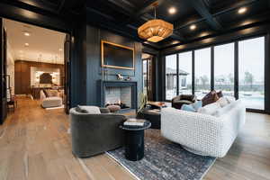 Living room with a warm lit fireplace, coffered ceiling, recessed lighting, light wood finished floors, and crown molding