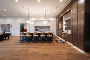 Kitchen with a large island, a kitchen breakfast bar, decorative light fixtures, open shelves, and light wood-style flooring