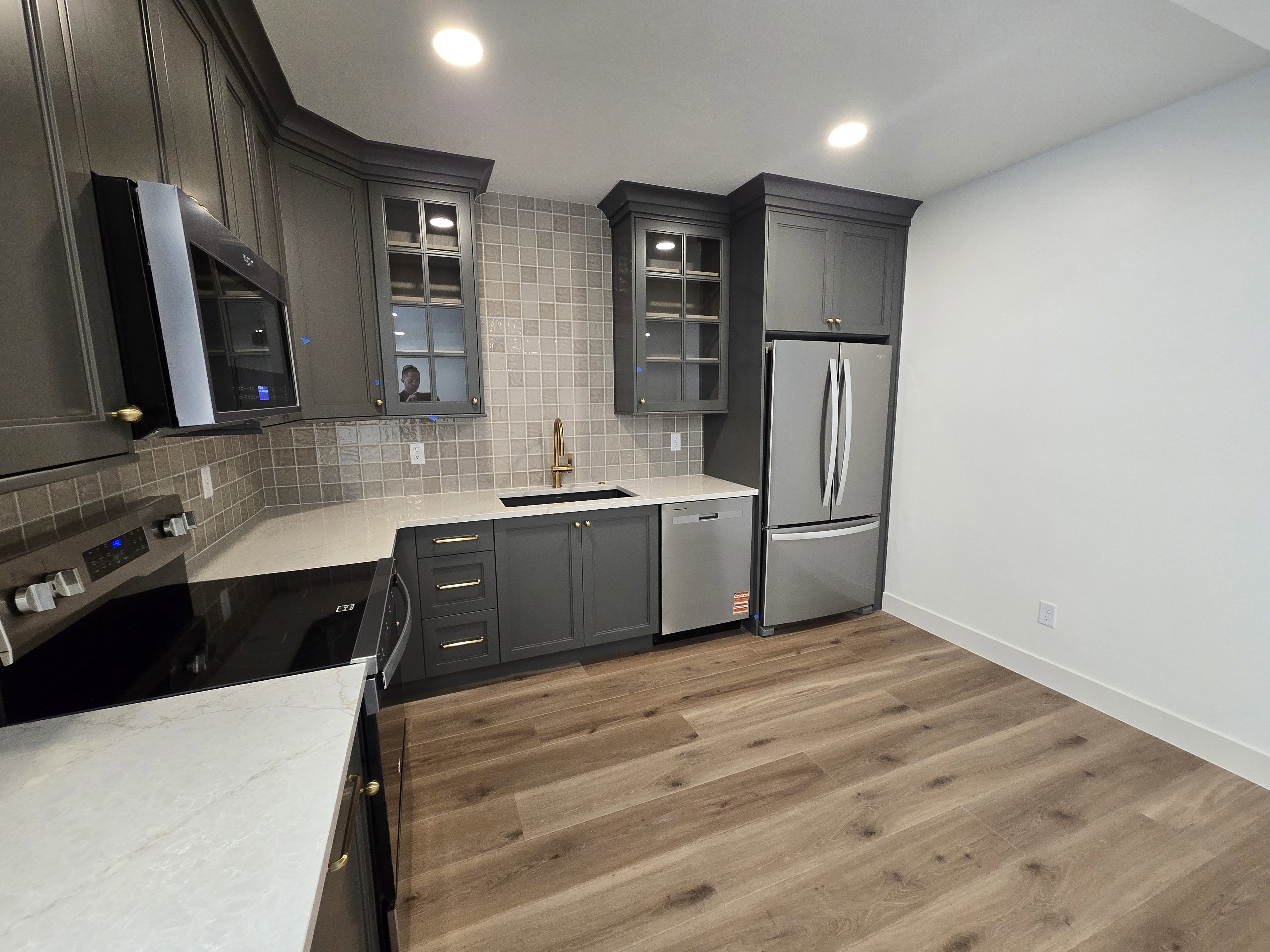 Contemporary kitchen featuring dark gray cabinetry with gold-toned hardware, quartz countertops, and a full suite of stainless steel appliances
