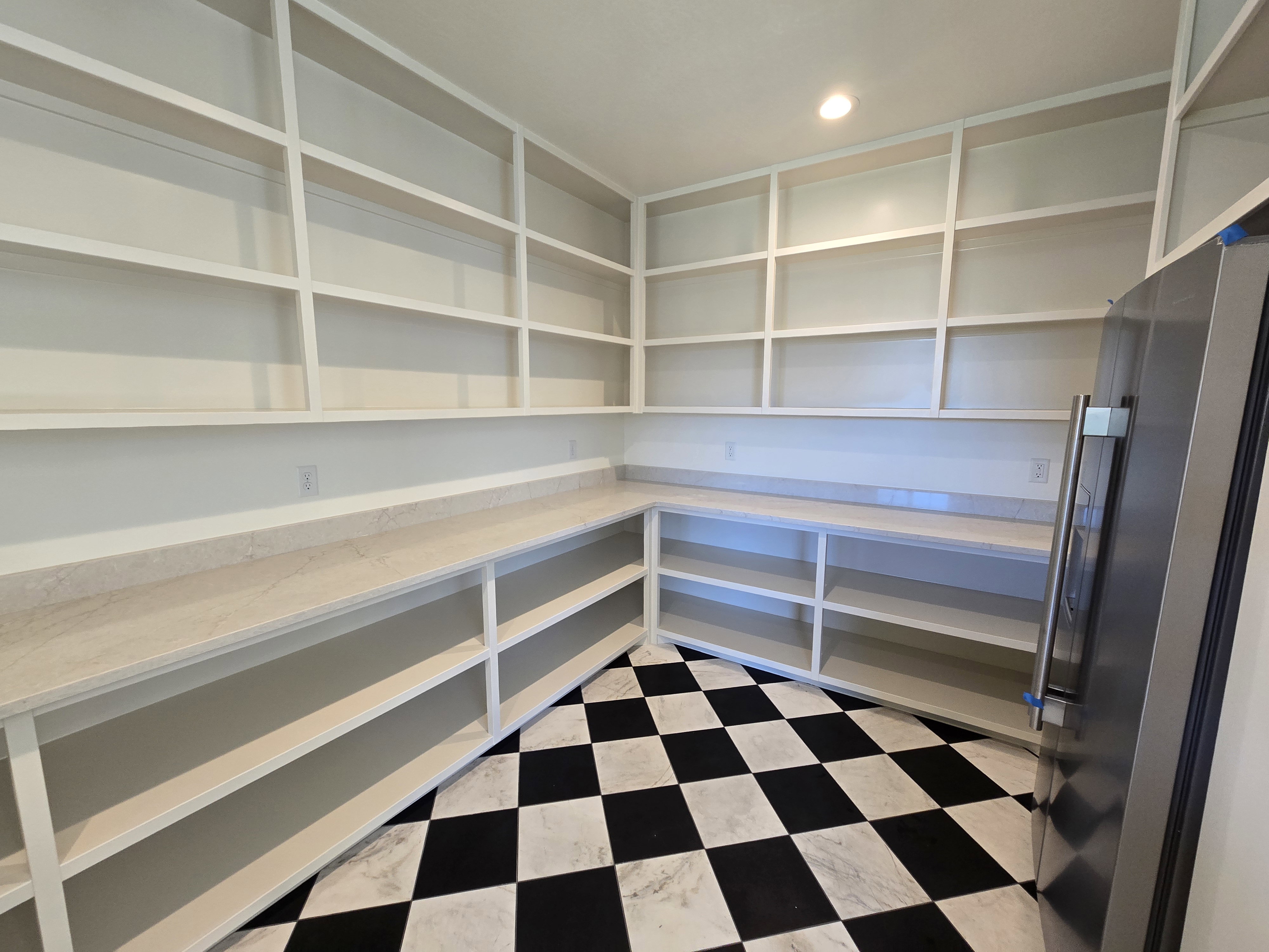 Spacious pantry featuring extensive built-in shelving, ample countertop space, checkerboard tile flooring, recessed lighting, and a stainless steel refrigerator