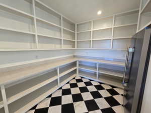 Spacious pantry featuring extensive built-in shelving, ample countertop space, checkerboard tile flooring, recessed lighting, and a stainless steel refrigerator