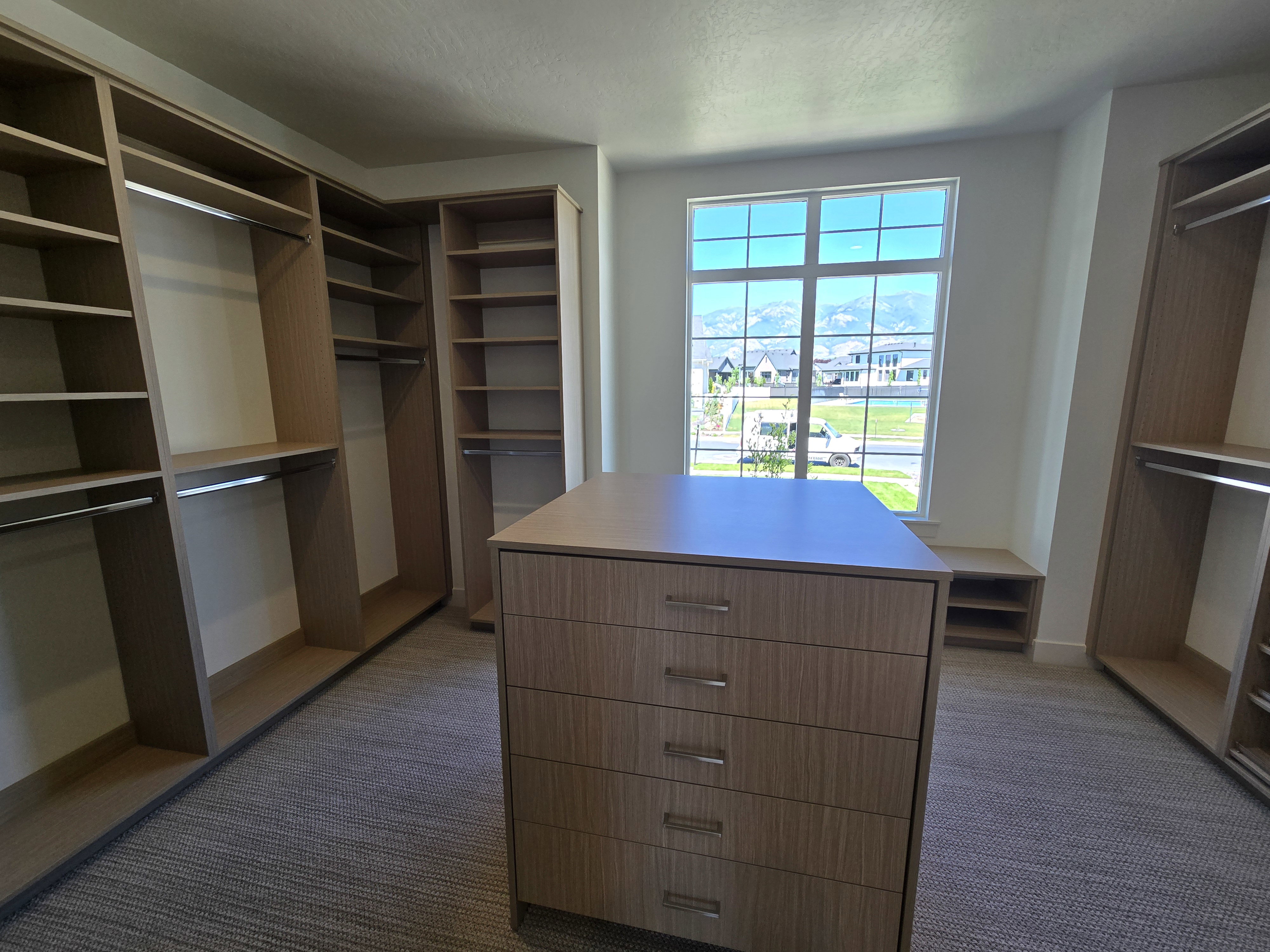 Spacious walk-in closet featuring extensive built-in shelving, multiple hanging rods, and a central island with integrated drawers