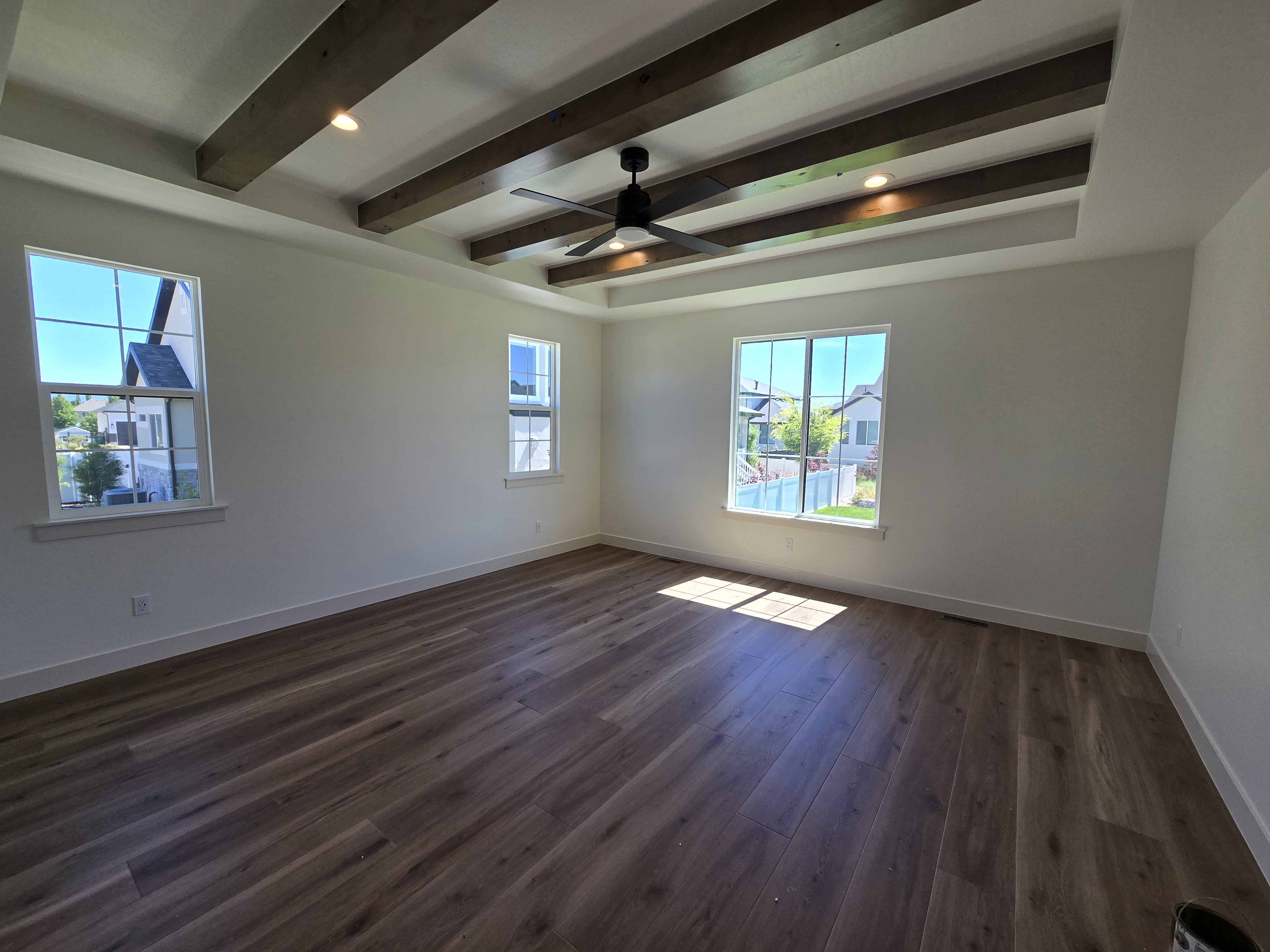 Spacious room featuring a tray ceiling with exposed wood beams, a ceiling fan, recessed lighting, and wood-finish flooring