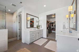 Bathroom featuring a walk in closet, two vanities, a shower stall, and recessed lighting