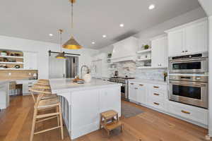 Kitchen featuring open shelves, white cabinets, a barn door, light wood-style flooring, and stainless steel appliances