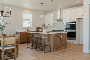 Kitchen with dual tone cabinetry, a kitchen bar, double oven, light wood finished floors, and a kitchen island