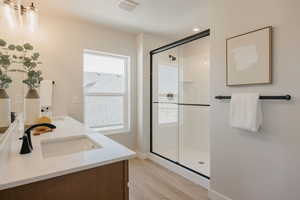 Full bathroom featuring a shower stall, double vanity, and light wood-style flooring