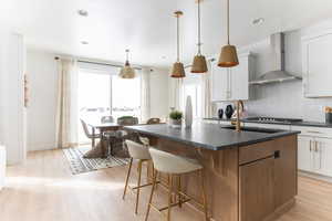 Two tone kitchen with an island with sink, tasteful backsplash, a kitchen breakfast bar, light wood-type flooring, and pendant lighting