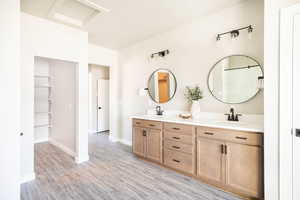Full bathroom with double vanity, light wood finished floors, and a walk in closet