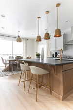 Kitchen with a kitchen breakfast bar, hanging light fixtures, two tone cabinets, light wood finished floors, and backsplash