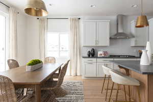 Kitchen with dark countertops, hanging light fixtures, light wood-style flooring, backsplash, and a kitchen bar