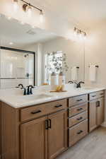 Full bathroom with double vanity, a stall shower, and light wood-style flooring
