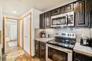 Kitchen featuring stainless steel appliances, dark wood finish cabinets, backsplash, and tile counters