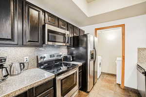 Kitchen featuring stainless steel appliances, dark wood finish cabinets, light stone finish floors, tasteful backsplash, and tile countertops