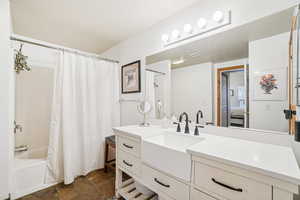 Full bath with shower / tub combo with curtain, vanity, and dark stone finish flooring