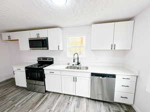 Kitchen with stainless steel appliances, white cabinetry, light countertops, light wood-style flooring, and a textured ceiling