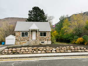 View of front facade featuring a mountain view, stone siding, an outdoor structure, and a detached garage