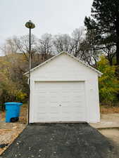 Detached garage featuring asphalt driveway and view of scattered trees