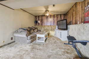 Carpeted living room with a textured ceiling, ceiling fan, and wood walls