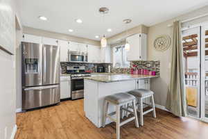 Kitchen with pendant lighting, stainless steel appliances, a breakfast bar, and light wood-type flooring