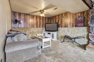 Carpeted living area with a ceiling fan, a textured ceiling, and wooden walls