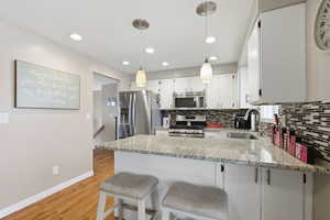 Kitchen with stainless steel appliances, hanging light fixtures, white cabinetry, a breakfast bar area, and light stone counters