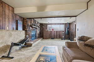 Carpeted living area featuring a textured ceiling, wooden walls, and a stone fireplace