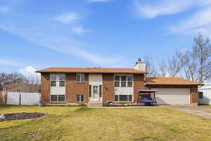 Bi-level home featuring concrete driveway, a chimney, brick siding, and a garage
