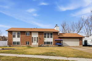 Raised ranch featuring a front lawn, driveway, a chimney, brick siding, and a garage