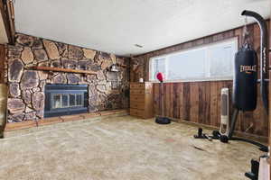 Carpeted living area featuring wood walls, a stone fireplace, and a textured ceiling