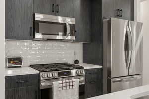 Kitchen featuring modern cabinets, stainless steel appliances, light stone countertops, and backsplash