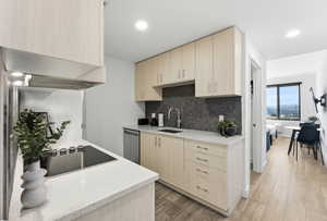 Kitchen with light wood finish cabinetry, light stone counters, light wood-type flooring, black electric cooktop, and tasteful backsplash