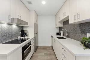 Kitchen featuring black appliances, light stone counters, light wood-style floors, and tasteful backsplash