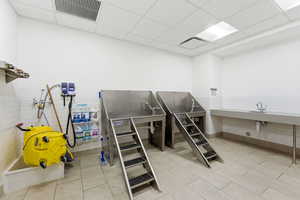 Misc room featuring a paneled ceiling, tile walls, a wainscoted wall, pet washing area, and light tile patterned flooring