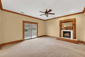 Unfurnished living room with crown molding, a fireplace, carpet floors, and ceiling fan