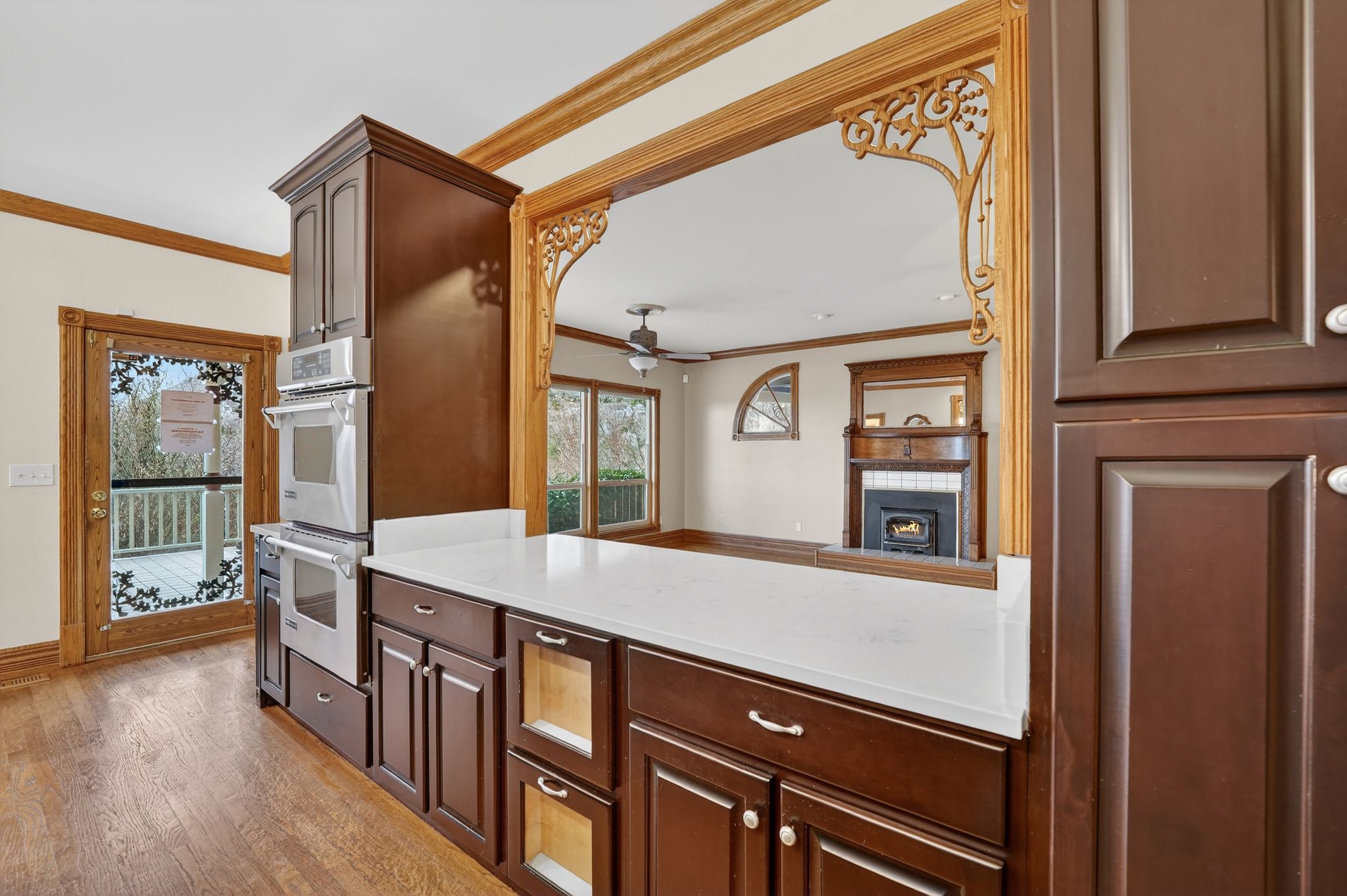Kitchen featuring crown molding, ceiling fan, stainless steel double oven, light wood-style floors, and dark brown cabinetry
