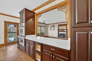 Kitchen featuring crown molding, ceiling fan, stainless steel double oven, light wood-style floors, and dark brown cabinetry