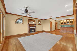 Unfurnished living room featuring a tile fireplace, ornamental molding, and light wood-type flooring