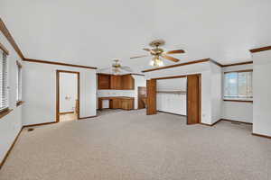 Unfurnished living room with light colored carpet, crown molding, built in desk, and ceiling fan