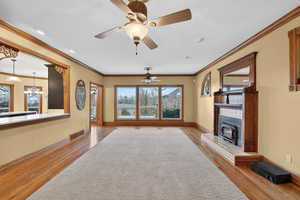 Unfurnished living room featuring ornamental molding, a ceiling fan, light wood-style floors, a chandelier, and a tile fireplace