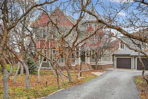 Obstructed view of property featuring covered porch, a garage, a shingled roof, and driveway