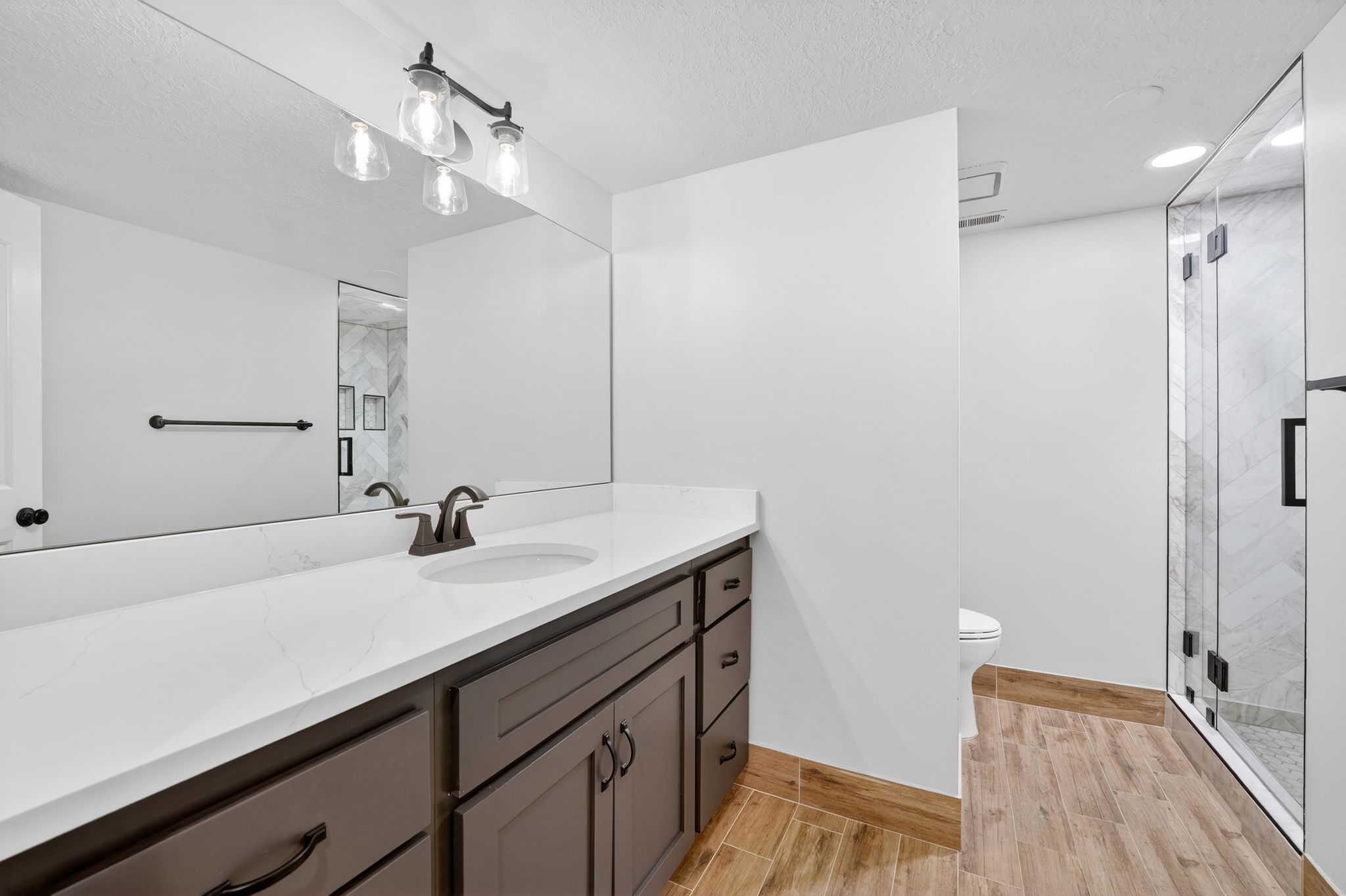 Bathroom with vanity, a marble finish shower, a textured ceiling, and wood tiled floors