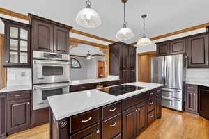 Kitchen with a kitchen island, dark brown cabinets, appliances with stainless steel finishes, light wood-type flooring, and crown molding