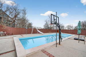 View of pool with a water slide, a fenced backyard, and a patio area